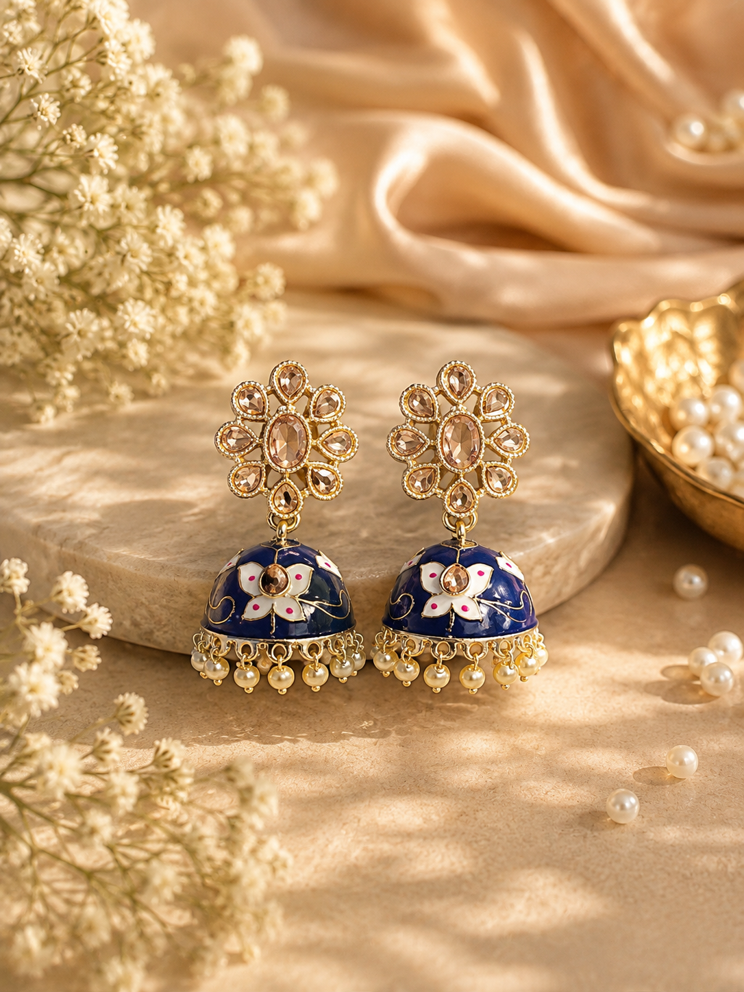 Blue meenakari jhumka earrings with gold-tone floral stud, enamel dome with floral motifs, and faux pearl drops