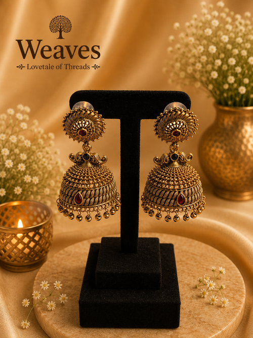 Antique Gold Granule Jhumka Earrings with ruby red teardrop accent and gold bead drops on black earring stand