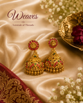 Ornate gold-tone jhumka earrings with red and green accent stones and dangling bead drops
